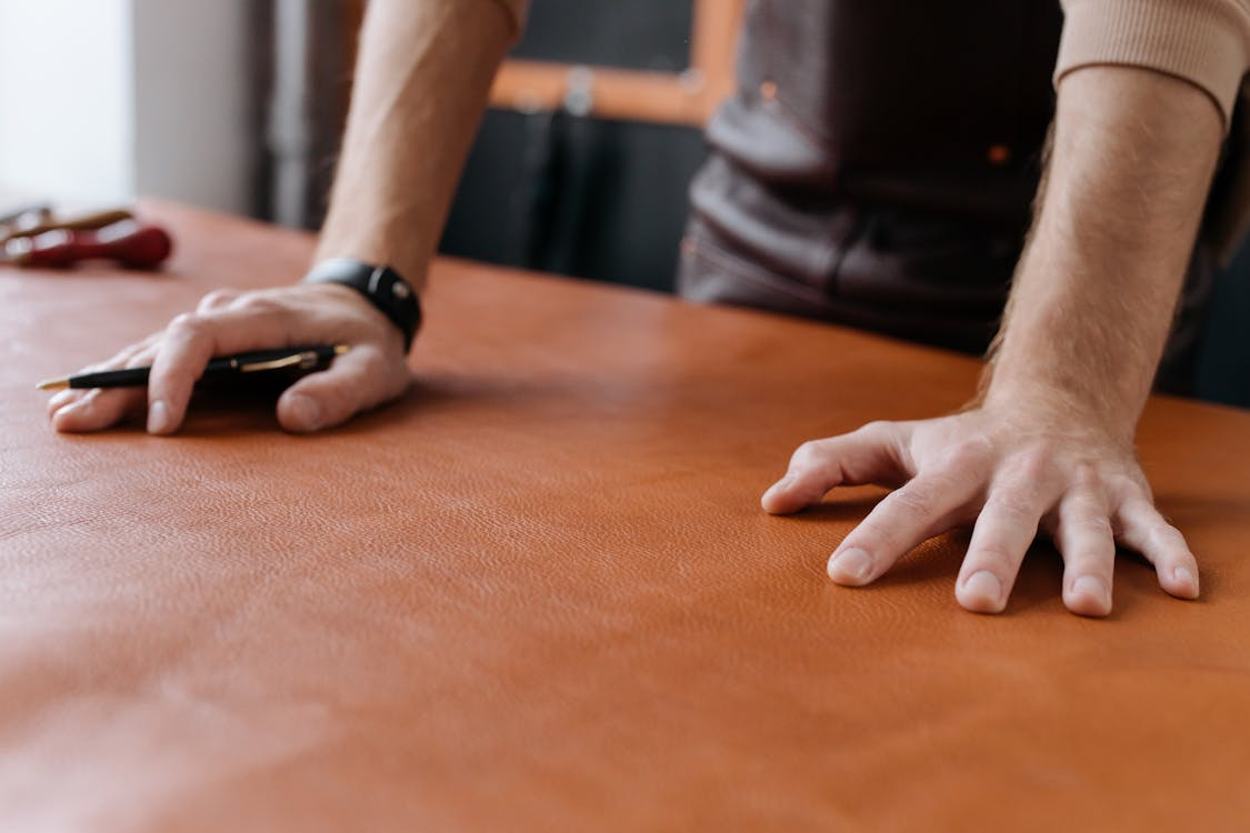 close up of man standing with his hands on the table with a sheet of brown leather