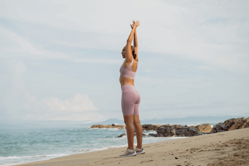 An image of a woman wearing sportswear, stretching on the beach