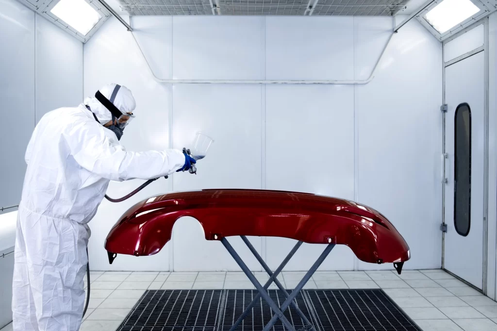 a person using a spray gun to coat the car component